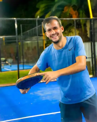 Un jugador de pádel sonríe con la paleta en la mano, de noche, en la cancha.
